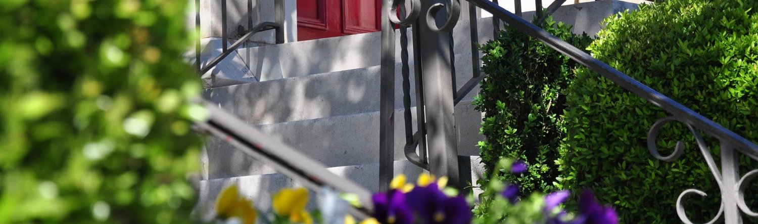 artistic photo of exterior stairing with landscaping and metalwork leading to a red front door.