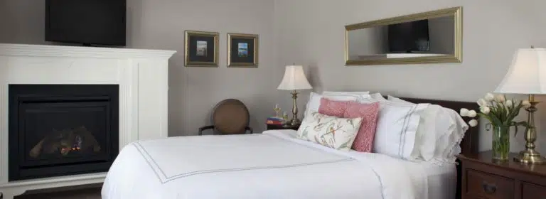 Bedroom with light taupe walls, dark wooden furniture, white bedding, and fireplace