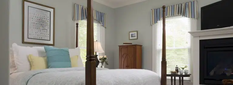 Bedroom with light green walls, white trim, dark wooden four poster bed, light colored bedding, and fireplace