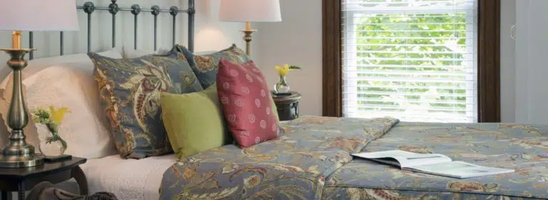 Bedroom with light-colored walls, dark wooden trim, blueish gray painted wrought iron headboard, and multicolored bedding