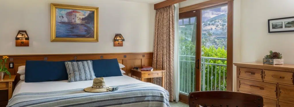 Bedroom with wooden bed, light-colored bedding with navy pillows, wooden nightstands, and garden view